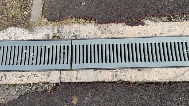 Closeup stadium track drainage grate metal, curved galvanized grating set into curb between rubber track and asphalt, visible seam