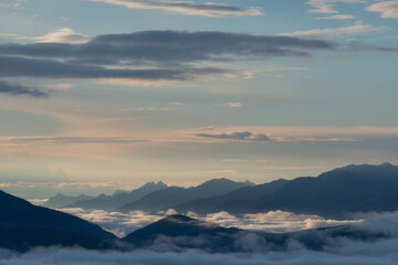 Fototapeta premium Tranquil mountain range shrouded in mist under a soft sunrise sky. Ideal for wellness, travel, and environmental backgrounds.