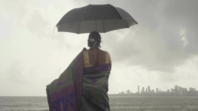 Young Indian woman in a saree holding an umbrella by the beach in Mumbai, India
