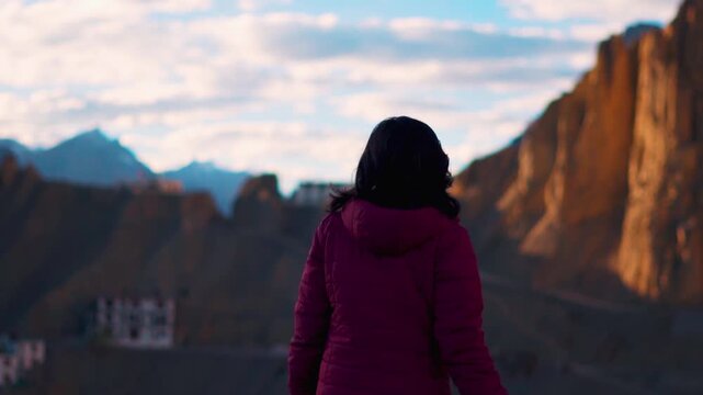 Rear view of Indian female tourist walking in front of Dhankar Monastery in Spiti Valley, Himachal Pradesh, India. Young Indian woman travel and explore mountains. Travel lifestyle, budget trip and ba