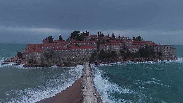 Drone Pull-Away from Sveti Stefan Island in Overcast Weather with Crashing Sea Waves, Montenegro