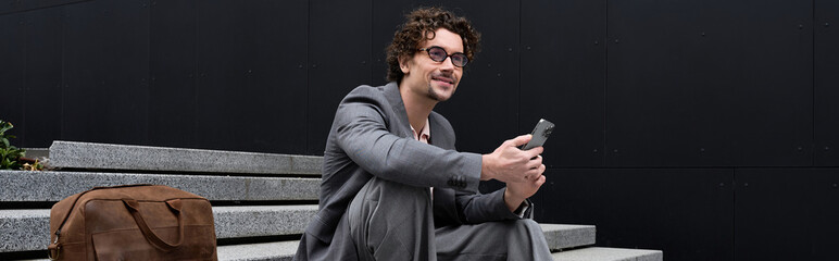 Obraz premium Handsome man with curly hair dressed elegantly enjoys a moment on the street steps