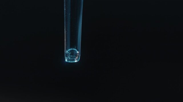 Liquid dripping from pipette on black background