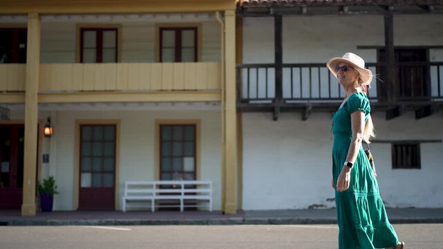 A happy senior woman walks next to the Sonoma Barracks and Toscano Hotel in California on a bright morning after sunrise.