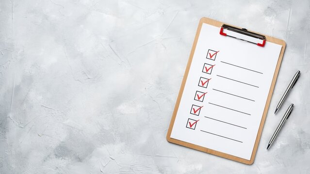 Clipboard with checklist, red check marks and pens on grey stone background