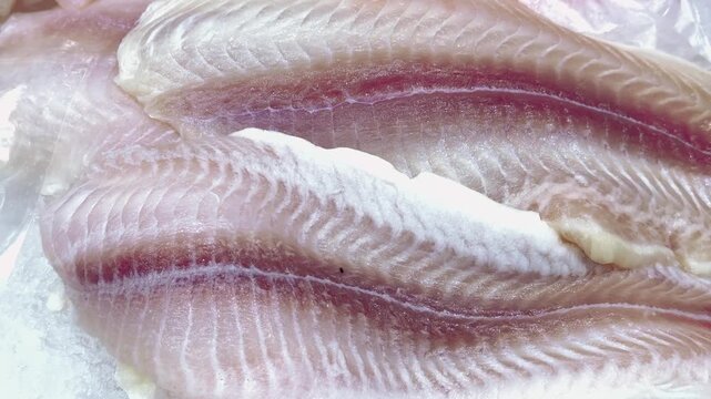 Fresh cod fillets and Pangasius fillet on crushed ice, close-up of glistening flesh and pink bloodline on market counter, vendor preparing portions