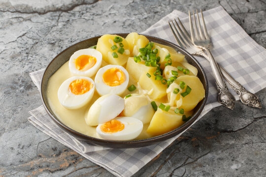 Close-up of hard-boiled eggs in mustard sauce with a side dish of boiled potatoes in a plate on the table. Horizontal