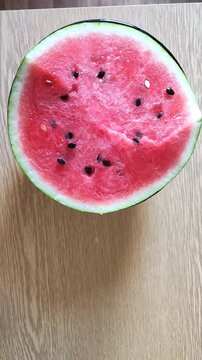 Fresh ripe watermelon cut in half with red flesh and black seeds on wooden surface, summer fruit.