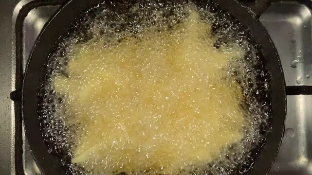 Close up of French fries cooking in a pan on an uncleaned gas stove
