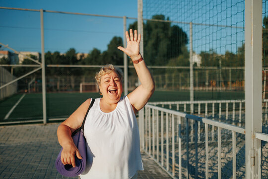 Joyful large pensioner waving hand before morning fitness routine.