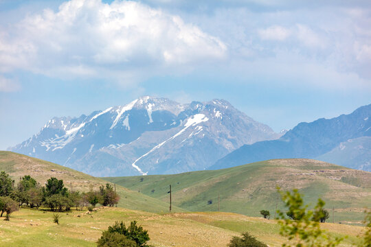 Snow-capped mountains rise behind rolling green hills