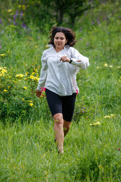 Woman runs through green grass with wildflowers. She wears light jacket and dark shorts. Her hair flows as she moves forward.