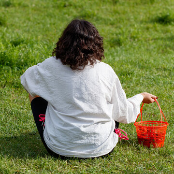Woman sits on grass holding orange basket