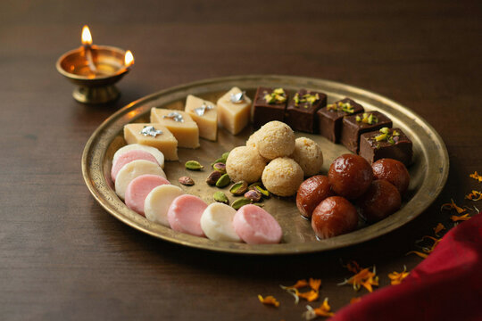A beautiful brass plate holds an exquisite assortment of traditional Indian sweets featuring gulab jamun ladoo barfi and peda creating a vibrant delicious festive dessert platter for celebration