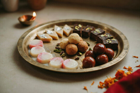 A beautiful brass plate holds an exquisite assortment of traditional Indian sweets featuring gulab jamun ladoo barfi and peda creating a vibrant delicious festive dessert platter for celebration