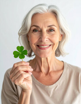Mujer senior sonriente sosteniendo un tr&eacute;bol de cuatro hojas, s&iacute;mbolo de suerte, felicidad, bienestar y envejecimiento saludable con calidad de vida, optimismo, esperanza y longevidad en la madurez