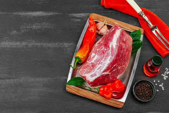 Raw pork loin on a metal tray with chili peppers, garlic, bay leaves, oil, and spices