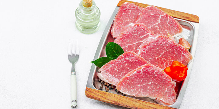 Sliced raw pork loin on a metal serving tray with garlic, chili pepper, and bay leaves on a white