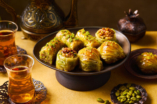 Turkish baklava desserts with pistachios and walnuts served with tea on yellow background. Close up.