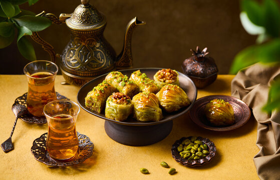 Delicious arabic dessert composition with honey pistachio baklava and armudu tea cups. Yellow and brown background. Close up.