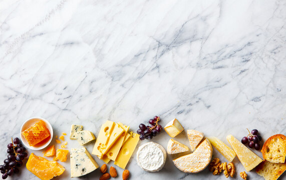 Assorted of cheese with grapes, nuts and honey on a marble board. Grey background. Copy space. Top view.