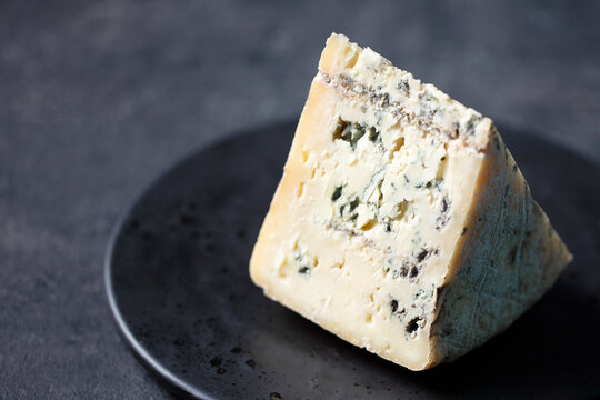 Gorgonzola cheese block on black plate with copy space ready for gourmet food design. Dark grey background. Close up.
