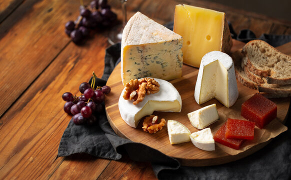 Cheese board with quince paste, red grapes nuts on rustic wooden table. Brown background. Close up.