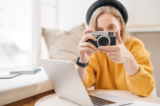 Female photographer taking a photo with camera while working on laptop
