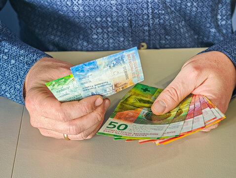 Man holding colorful 10, 20, 50 and 100 Swiss Francs bills planning travel budget or shopping trip