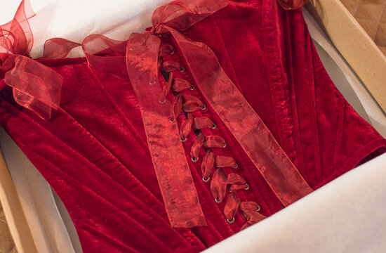 Luxurious deep red velvet corset top with off-the-shoulder straps and ribbon bows hanging on a hanger or lying in a gift box. Elegant feminine fashion lingerie garment with lacing detail