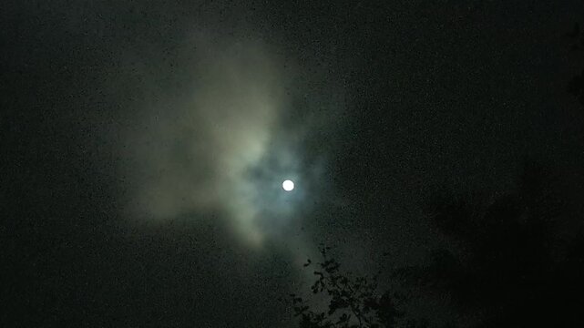 moody night sky time lapse featuring a bright moon behind dramatic clouds with heavy grain effect 