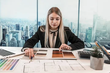 Female designer work at office with house plan for renovation, choose best color in wooden sampler © RomanR