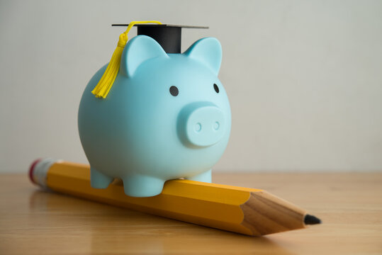 Piggy bank with mortarboard riding pencil on wooden table. Education, money savings and financial planning for education in university, college or study abroad, scholarship and so on concept.
