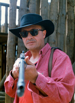 Cowboy in hat and sunglasses aiming rifle weapon