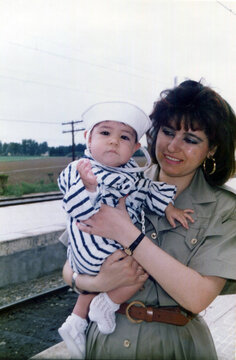 Mother holding baby wearing sailor outfit by train tracks
