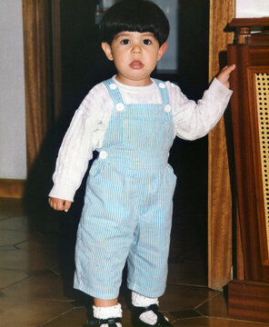 Toddler standing indoors wearing striped overalls looking curious