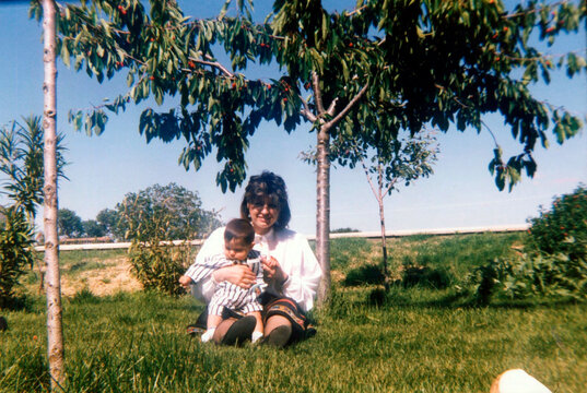 Mother holding baby sitting under a fruiting tree