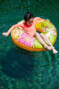 Little Chinese girl happily playing in a swimming pool with a swim r