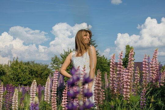Happy woman posing on flower meadow by blue sky with clouds