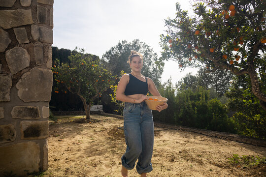 Woman carrying freshly picked oranges through a villa garden