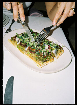 Dinner plate with hands cutting anchovy tart at restaurant