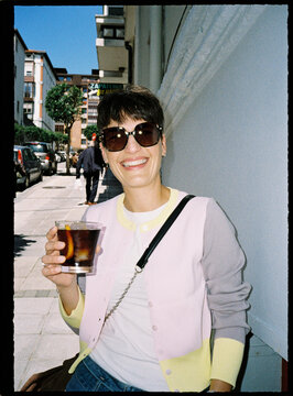 Smiling woman enjoying cocktail in city street on summer day