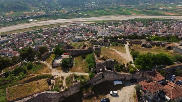 Sliding aerial drone view over the historic Berat Castle ruins and the modern city of Berat, Albania, revealing ancient fortress walls and scenic valley landscapes