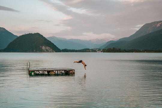 teenager diving from floating dock into calm alpine lake at dusk