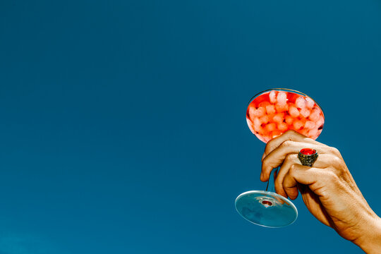 a man raises a red cocktail with ice to the blue sky