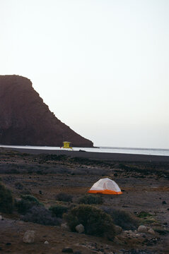 A lone tent set against a vast volcanic landscape at sunset.