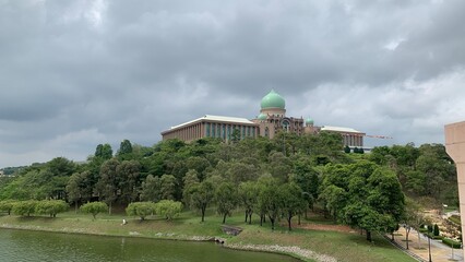 Government administrative complex with a green dome overlooking a lakeside landscape beneath dramatic storm clouds © MR HEPPY