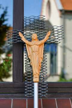 Geschnitzte Christusfigur aus Holz auf Kreuz aus Streckmetall vor Kirche