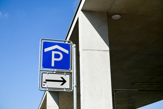 Blaues Parkhausschild mit Richtungspfeil vor moderner Betonkonstruktion