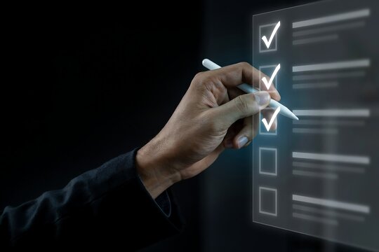 Hand using a stylus to check boxes on a transparent digital checklist interface in the darkness
